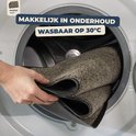 Hand die een beige deurmat in een wasmachine stopt. Wasbaar op 30°C.