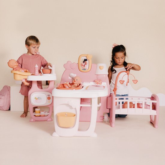 Jongen en meisje spelen met roze poppenverzorger. De jongen wast de pop, het meisje kijkt bij de wieg.