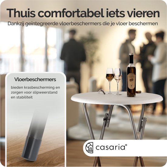 Table ronde blanche avec verres de vin et bouteille, sur un parquet. Pieds métalliques gris avec protecteurs de sol.