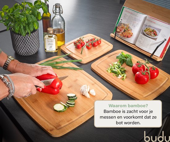 Bovenaanzicht van een vrouw die een rode paprika snijdt op een bamboe snijplank. Ingrediënten en een kookboek op de aanrecht.
