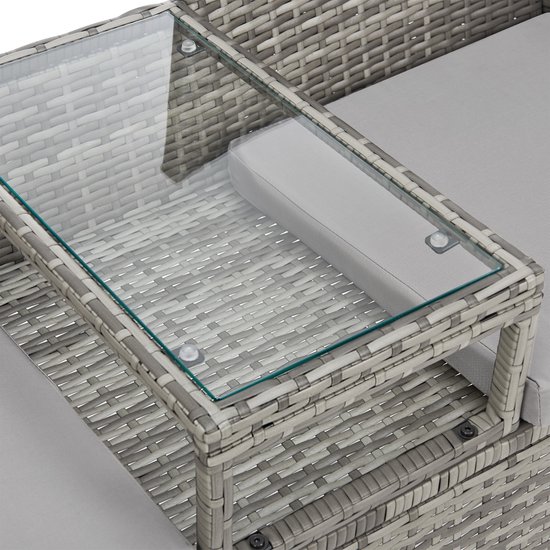 Detailopname van de glazen tafel in het midden van de grijze rotan tuinbank met lichtgrijze kussens.