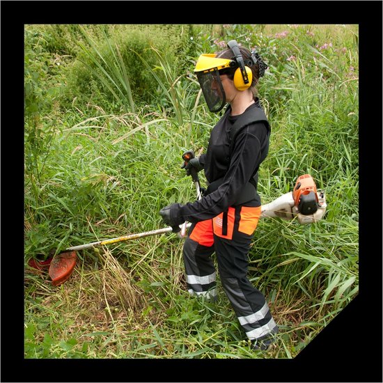Vrouw draagt beschermende kleding en gebruikt een bosmaaier in dichte vegetatie.