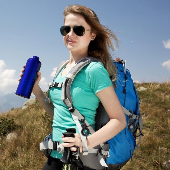 Een vrouw in wandelkleding met een rugzak en wandelstokken houdt een blauwe waterfles vast, met de bergen op de achtergrond.