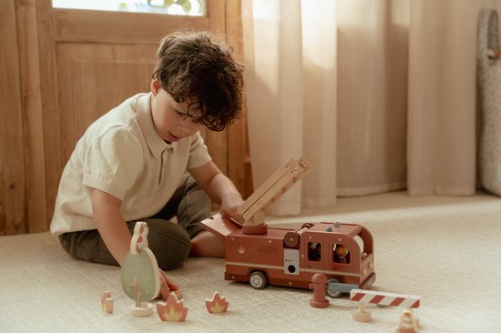 Kind speelt met houten brandweerwagen, ladder, boom, poppetjes, hydrant en vuurelementen.