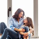 Vrouw en kind zittend bij een raam met bruine raamklink.