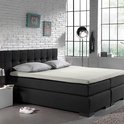 Donkergrijs bed met gestoffeerd hoofdbord, crème matras en twee kussens, in slaapkamer met witte muur.