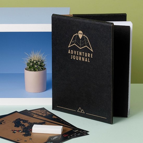 Een zwart reisdagboek met gouden letters, naast kaarten en een kleine cactus.