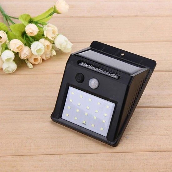 Zwarte V-TAC zonne-sensor wandlamp met 20 LED's, naast een bosje bloemen.