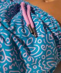 Detail van een turquoise zwembroek met een speels wit tekenpatroon en roze touwtjes met merkopdruk.