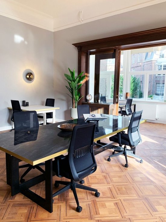 Een vergaderruimte met een zwarte tafel met gouden rand, zwarte bureaustoelen en houten vloer.