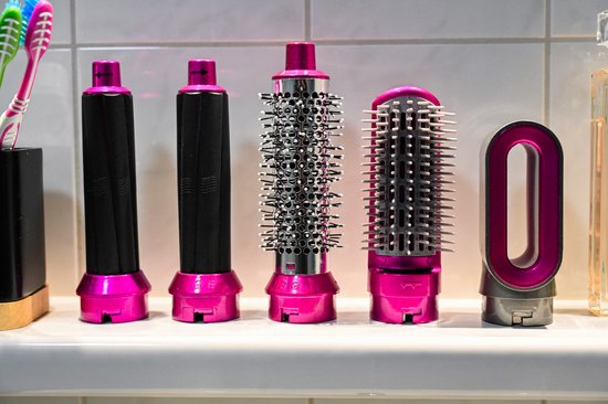 Verschillende opzetstukken voor een haarstyler, inclusief ronde borstels en een gladde opzetstuk, met roze accenten.