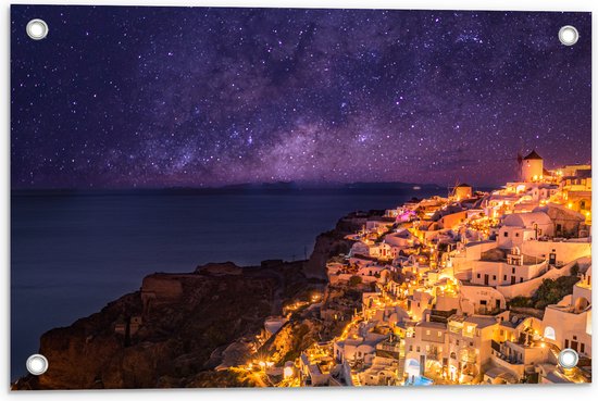 Tuinposter – Verlicht Dorp in de Nacht aan het water met de Melkweg in de Lucht - 60x40 cm Foto op Tuinposter (wanddecoratie voor buiten en binnen)