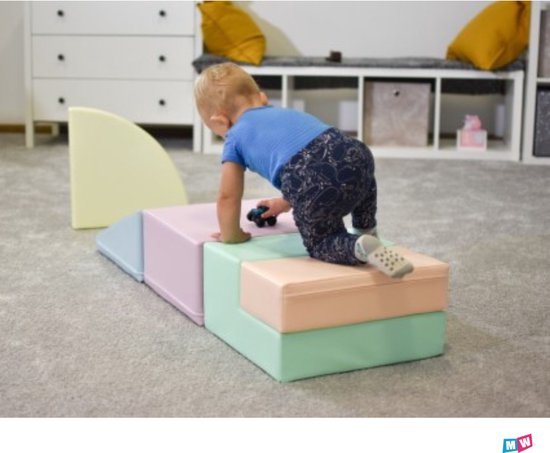 Un jeune enfant grimpe sur un ensemble de jeu souple aux couleurs pastel, avec une rampe bleu pastel et des blocs rose et bleu menthe.