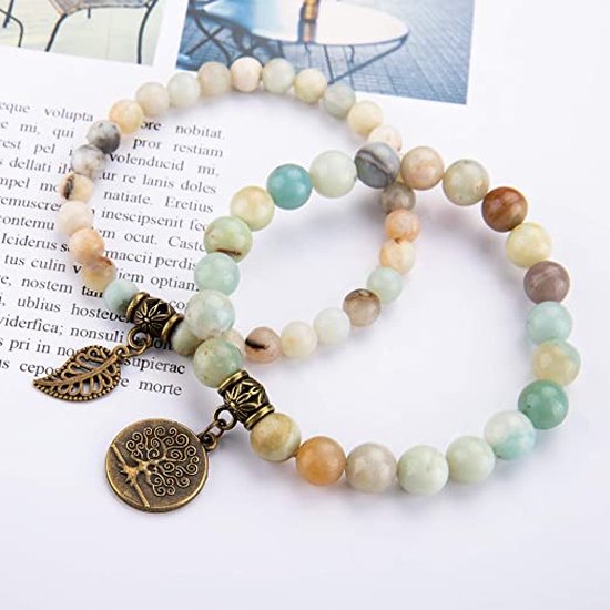 Twee armbanden van lichtgroene, beige en bruine kralen met bronzen bedels van een levensboom en een veertje, geplaatst op tekst.