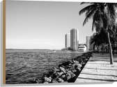 Hout - Palmbomen op het Strand met Uitzicht op Hoge Gebouwen Zwart/Wit - 80x60 cm - 9 mm dik - Foto op Hout (Met Ophangsysteem)