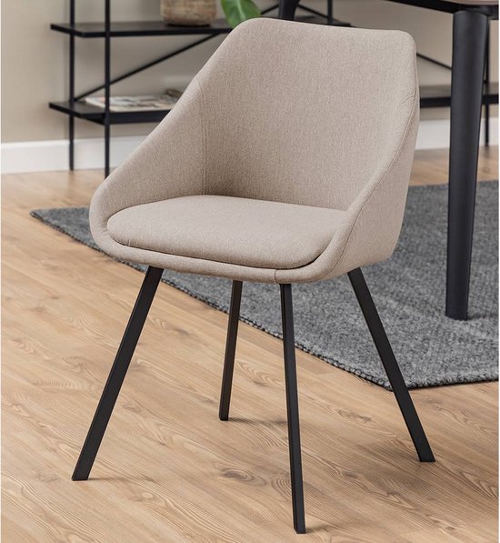 Chaise de salle à manger en tissu beige avec des pieds noirs inclinés sur un plancher en bois, à côté d'une table.