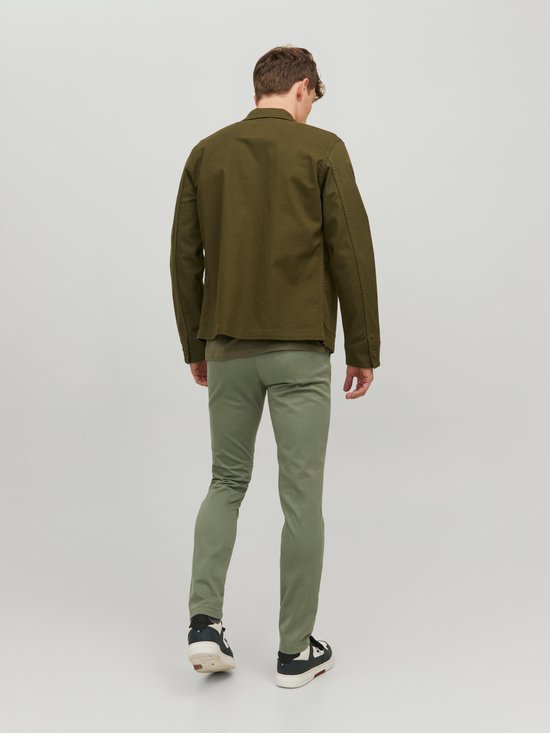 Man in lichtgroene chino en donkergroene jas, van achteren gezien.