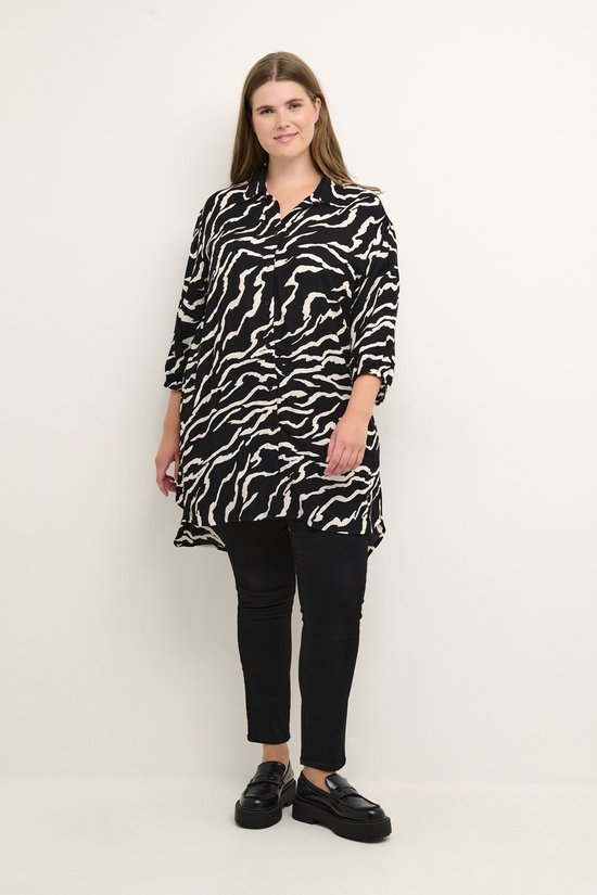 Vrolijke vrouw met lang bruin haar in een zwarte blouse met witte zebraprint en driekwartmouwen, gedragen met zwarte broek.