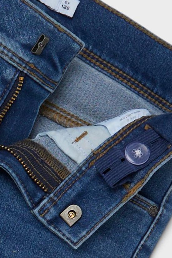Detail van de tailleband van een blauwe skinny jeans met knoop, rits en verstelbare elastiek.