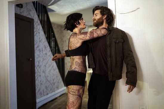 Vrouw met tatoeages en een man omhelzend in een huiselijke omgeving.