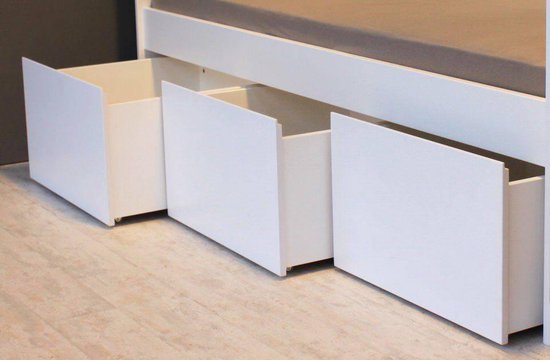 Onderkant van een wit bed met drie open lades.