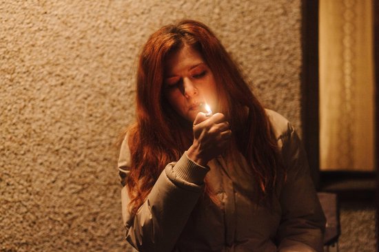 Vrouw met rood haar steekt sigaret aan met aansteker.