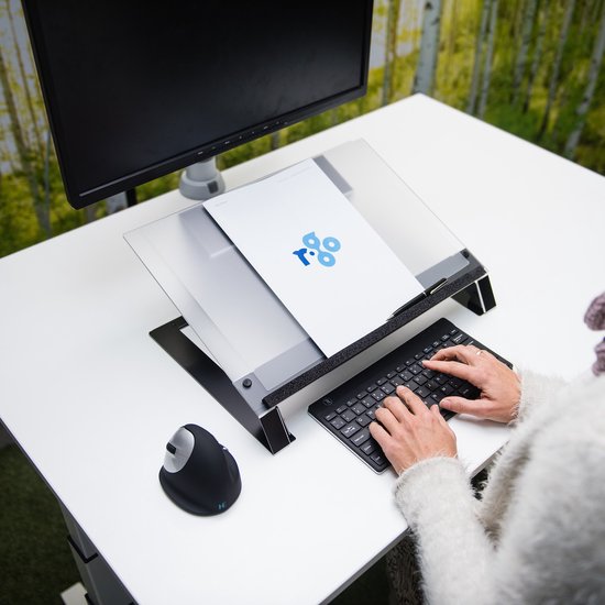 Zwarte documenthouder op een bureau met toetsenbord, muis en monitor. Een vrouw typt. Achtergrond met bosprint.