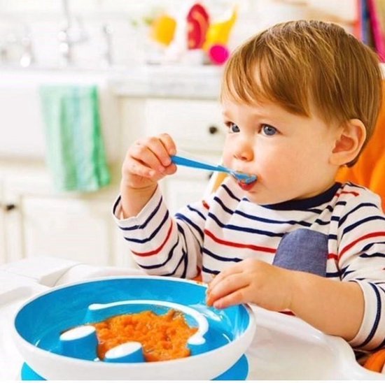 Een baby met gestreepte shirt eet pompoenpuree met een blauw-witte lepel uit een blauw smiley bord met zuignap.