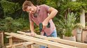 Man met bril en Bosch EasyDrill 18V-40 accuboormachine monteert houten balken.