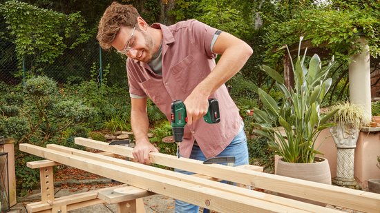 Man met bril en Bosch EasyDrill 18V-40 accuboormachine monteert houten balken.