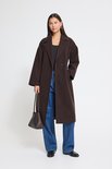 Model draagt een donkerbruine jas, blauwe jeans en draagt een gevlochten tas.