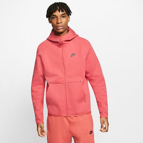 Model in koraalroze Nike Tech Fleece-hoodie met capuchon, Nike-logo duidelijk zichtbaar.
