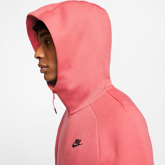 Zijaanzicht van model in koraalroze Nike Tech Fleece-hoodie, focus op capuchon en Nike-logo.