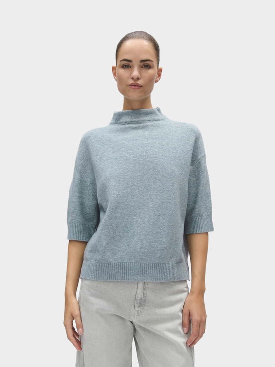 Model draagt een lichtblauwe, gebreide trui met opstaande kraag en driekwartmouwen.