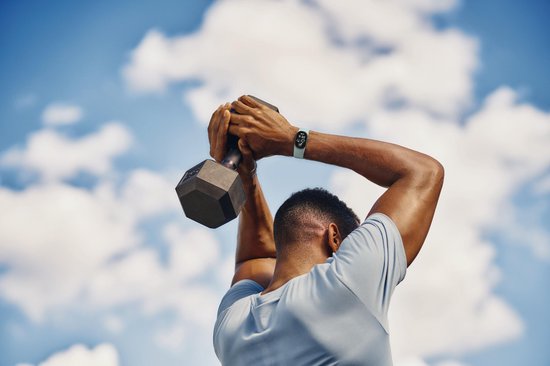 Man tilt een halter boven zijn hoofd met een lichtblauwe smartwatch om zijn pols.