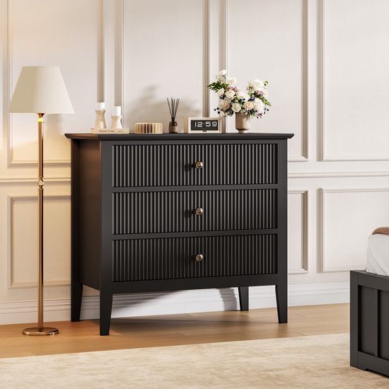 Commode noire à trois portes côtelées et boutons dorés. Une lampe sur pied se trouve à côté.