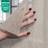Hand met bordeauxrode nagellak houdt lichtgrijze raamfolie met textielstructuur omhoog.