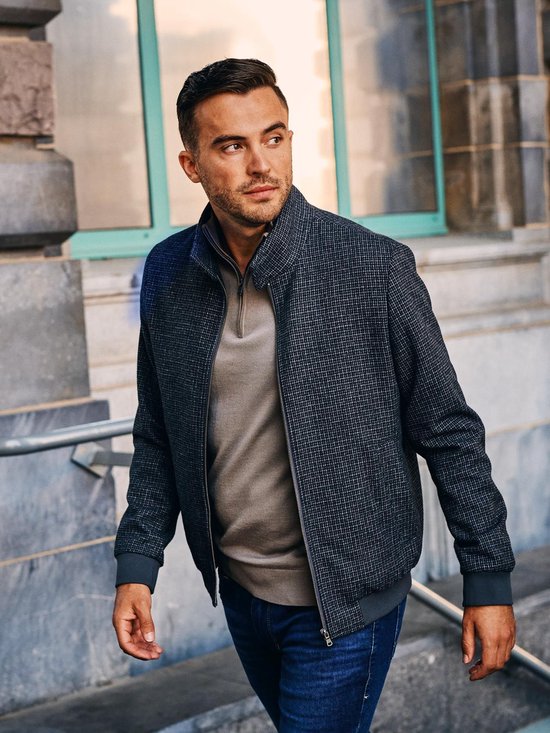 Model draagt een donkerblauw jack met pepita-motief, ritssluiting, en een taupe trui met halve rits.