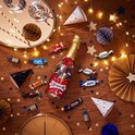 Celebrations-fles op een houten tafel met feestelijke verlichting, glazen, hoedjes en chocolade. Feestelijke sfeer.