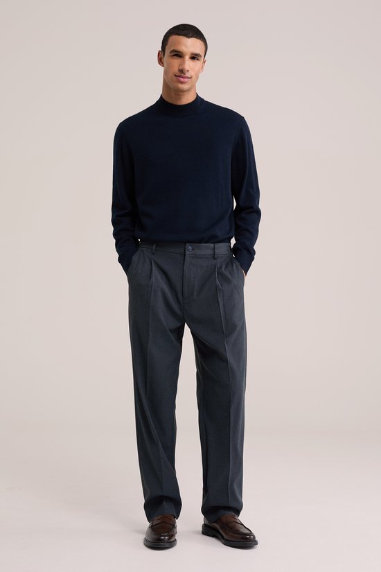 Man in donkerblauwe trui en donkerblauwe pantalon met bandplooi en bruine schoenen.