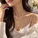 Een vrouw met lang bruin haar draagt een lange parelketting met gouden bloemhanger, over een satijnen top.