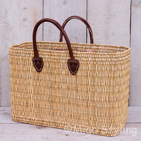Sac rectangulaire en osier marron clair avec poignées en cuir marron.