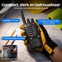 Zwarte portofoon in de hand boven bouwplannen, met oranje knoppen en de tekst 'Compact en eenvoudig mee te nemen'.