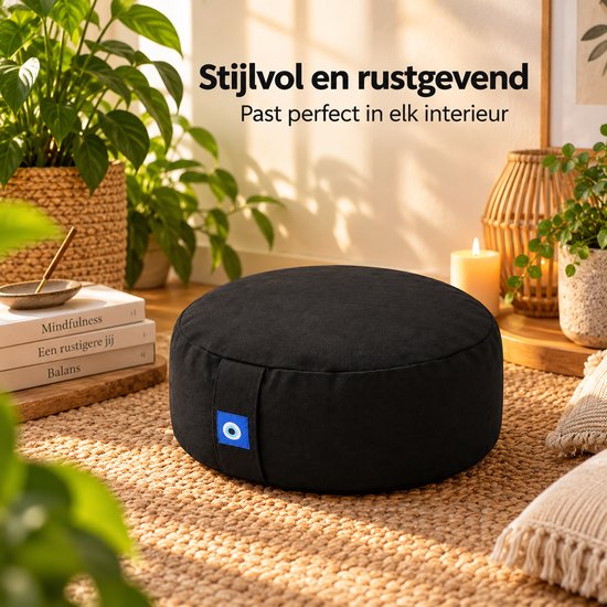 Zwart, rond meditatiekussen met een blauw oog-label, geplaatst in een sfeervol interieur.