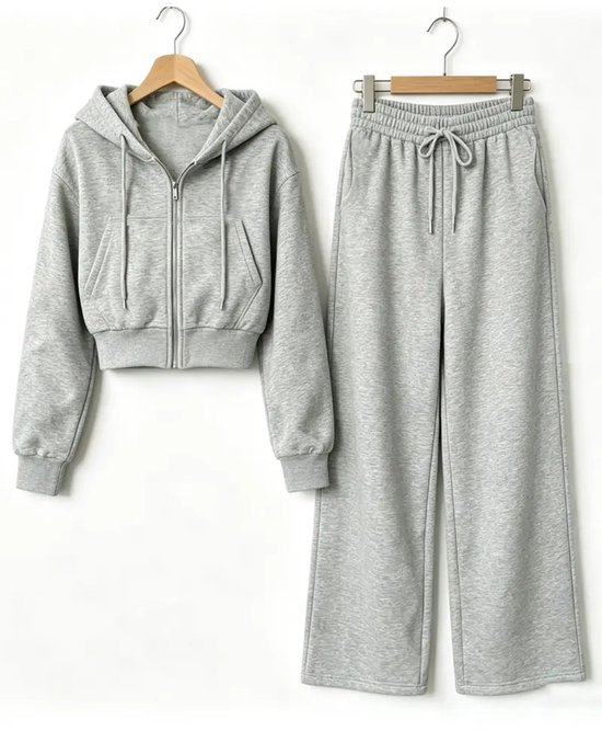 Grijze cropped hoodie met rits en bijpassende wijde joggingbroek, beide aan kledinghangers.