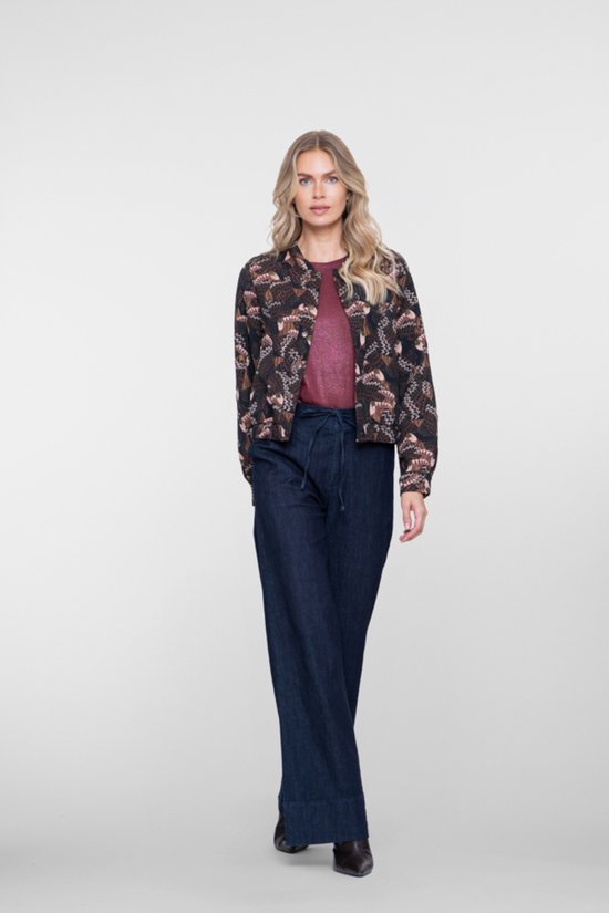 Model staat naar voren gericht, draagt een korte bomberjack met vogelprint en donkere jeans.