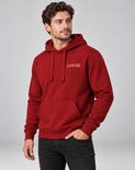 Man met donkere jeans, witte sneakers en rode COVAR hoodie met capuchon, staand.