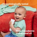 Baby met groene shirt en blauwe broek, vasthoudend aan tube Naïf crème met vlinderillustratie.