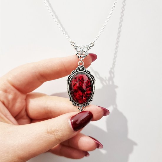 Hand houdt zilverkleurige ketting vast met een ovale hanger van gemarmerde rode steen.