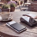 Zwarte MagSafe pasjeshouder op een telefoon naast een betaalterminal op een terras.